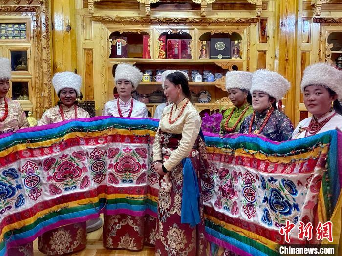 圖為女性展示村民自發(fā)繡制的“百米五彩哈達(dá)”?！±钣穹?攝
